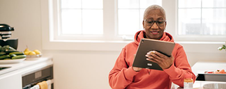image of an older woman looking at a tablet in her kitchen