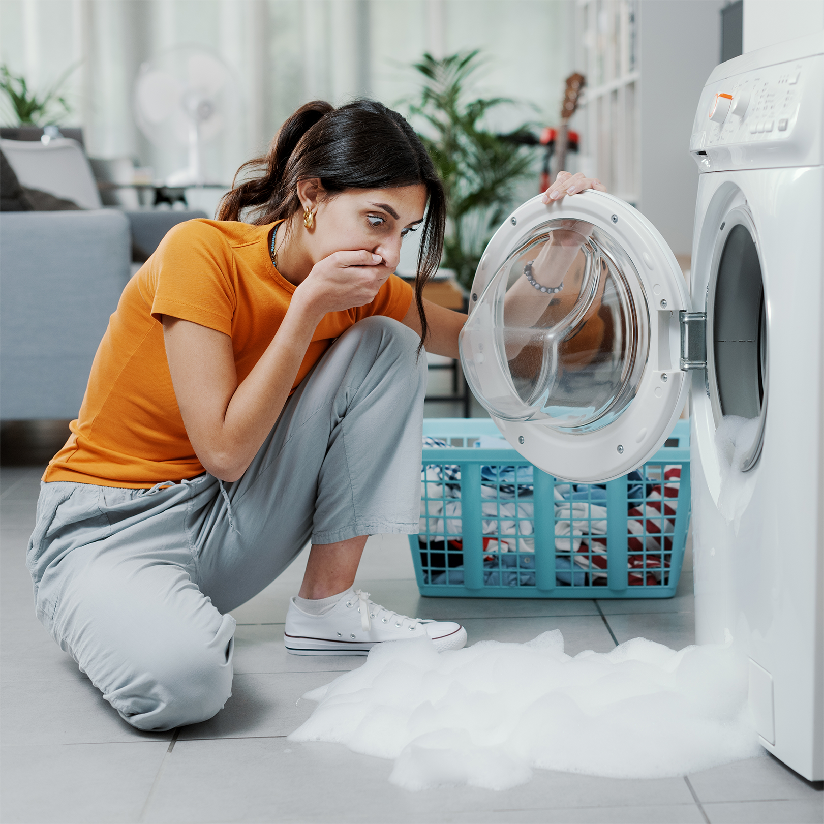 Woman checking her damaged washing machine, the floor is flooded.
