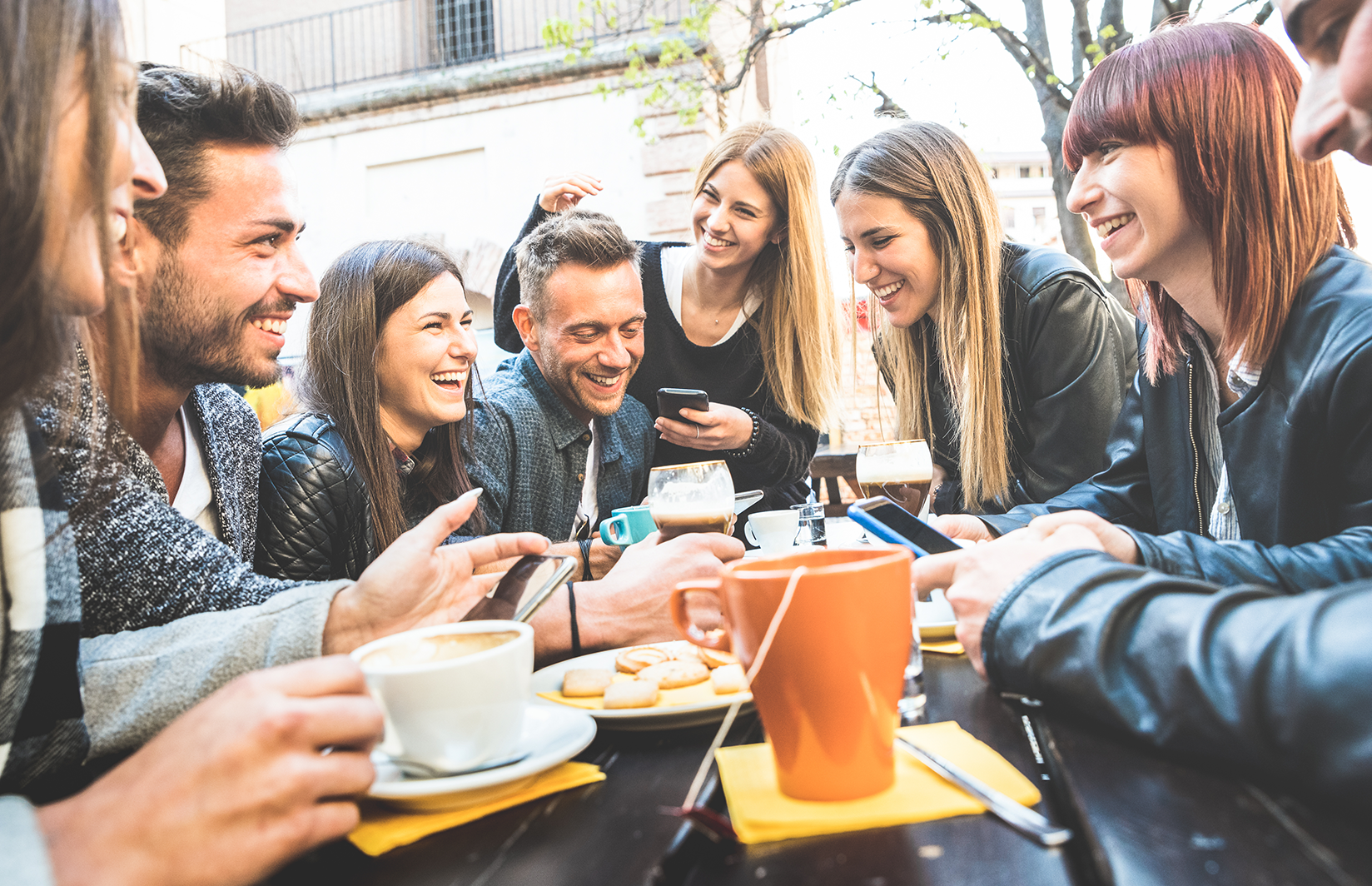 Happy friends talking and having fun with mobile smart phones at restaurant drinking cappuccino and hot tea.