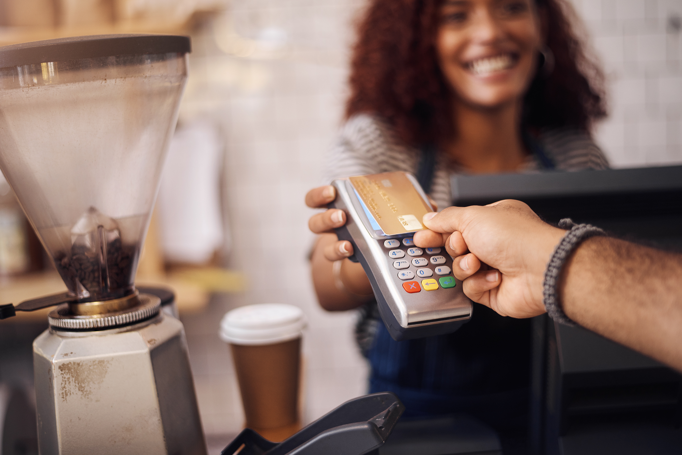 Person pays with a debit card at a POS machine at a coffee shop.