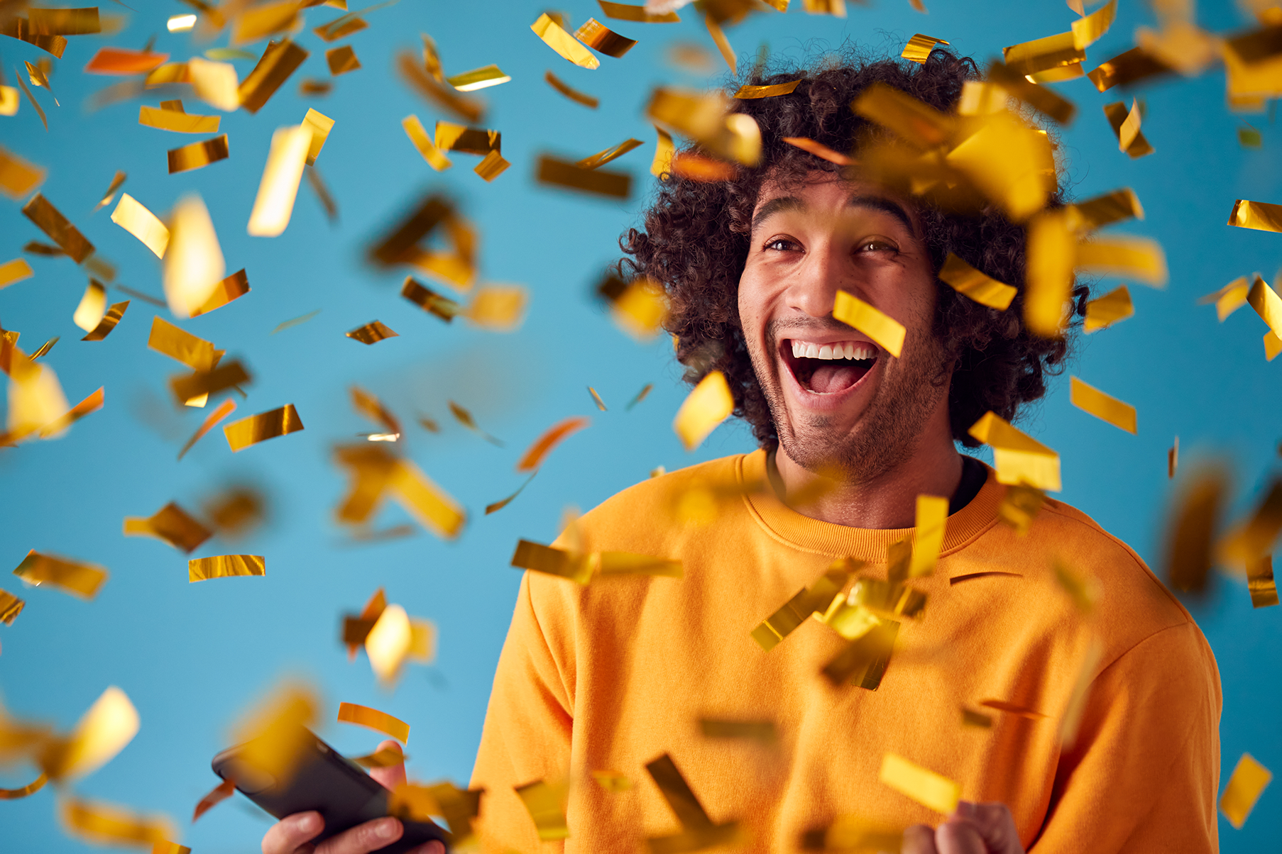 Celebrating Young Man With Mobile Phone Winning Prize And Showered With Gold Confetti.