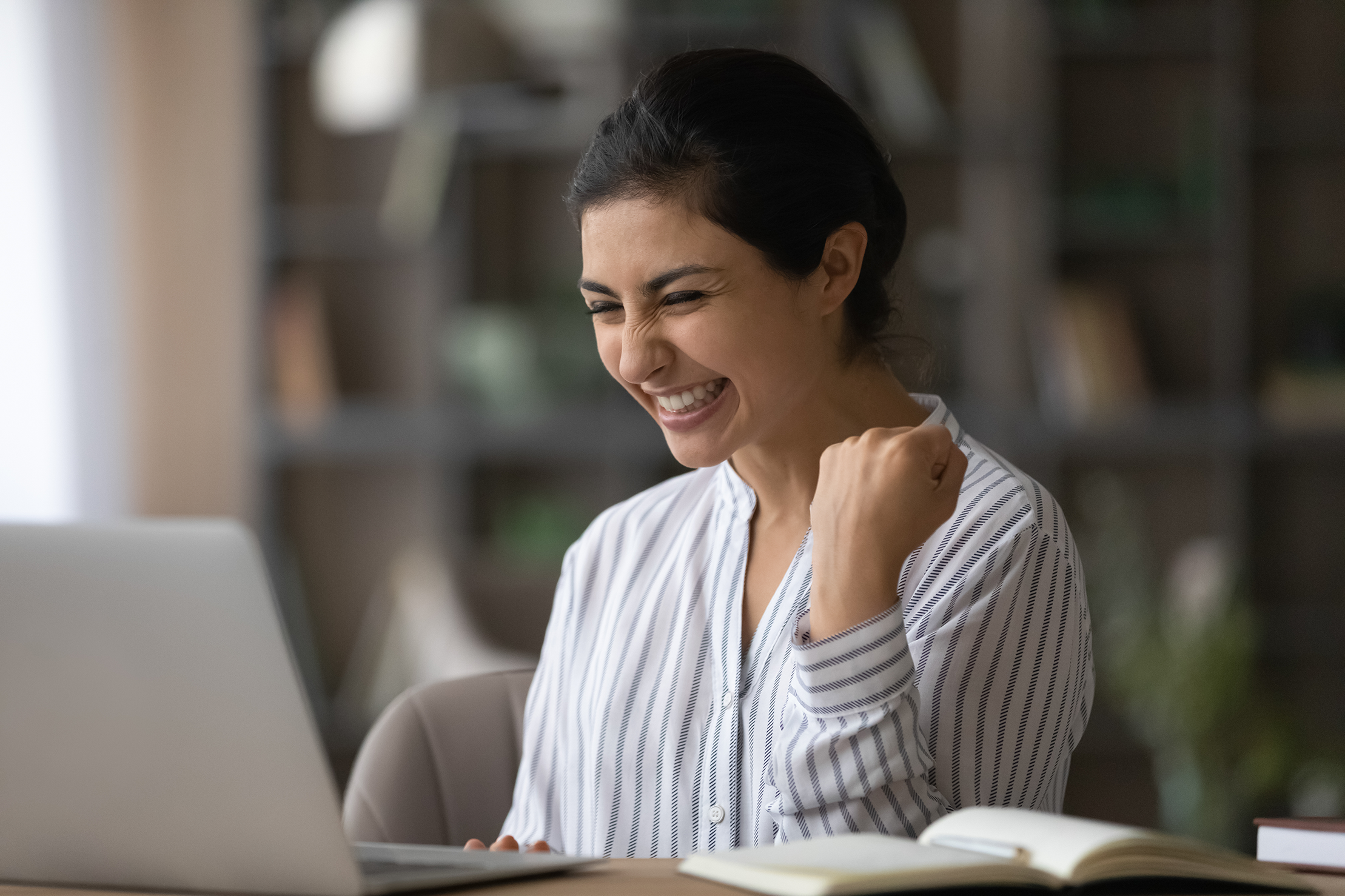 Excited millennial woman looks at computer screen in triumph.