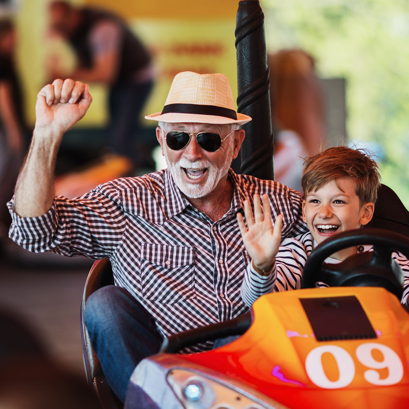 Grandfather and grandson having fun and spending good quality time together in amusement park. They enjoying and smiling while driving bumper car together.
